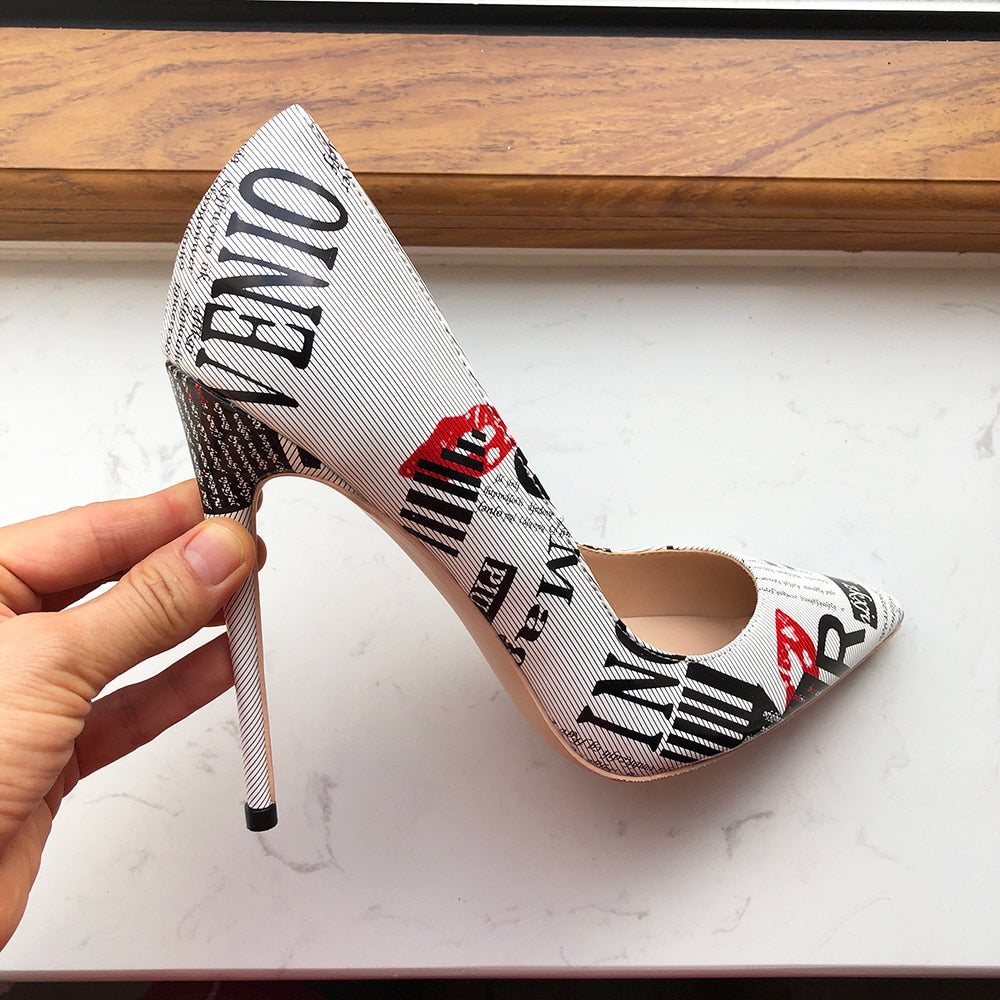 Hand displaying the Designer Graphic Newspaper Print Stiletto by its heel.